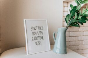 Framed quote 'Start each day with a grateful heart' next to a vase indoors.
